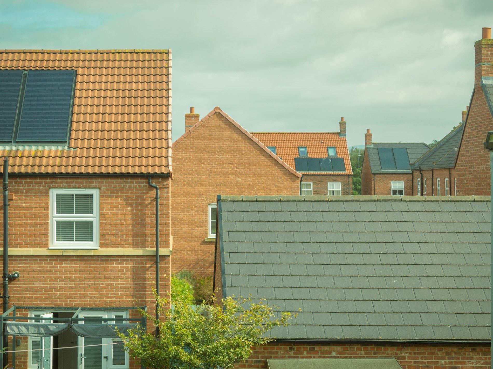 Rooftops of brick houses with solar panels and a conservatory below.