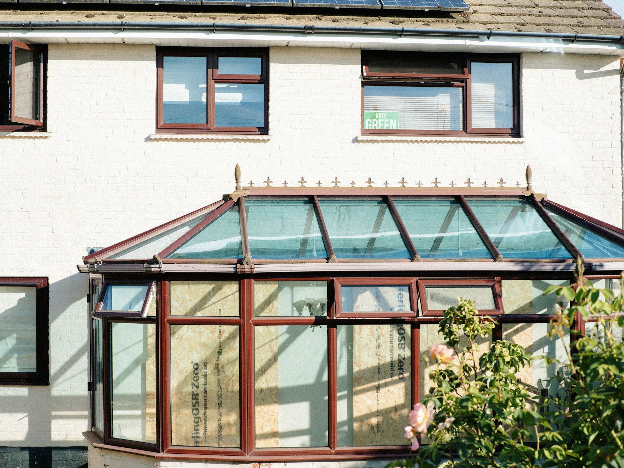 White semi-detached house with brown conservatory and solar panels on roof.